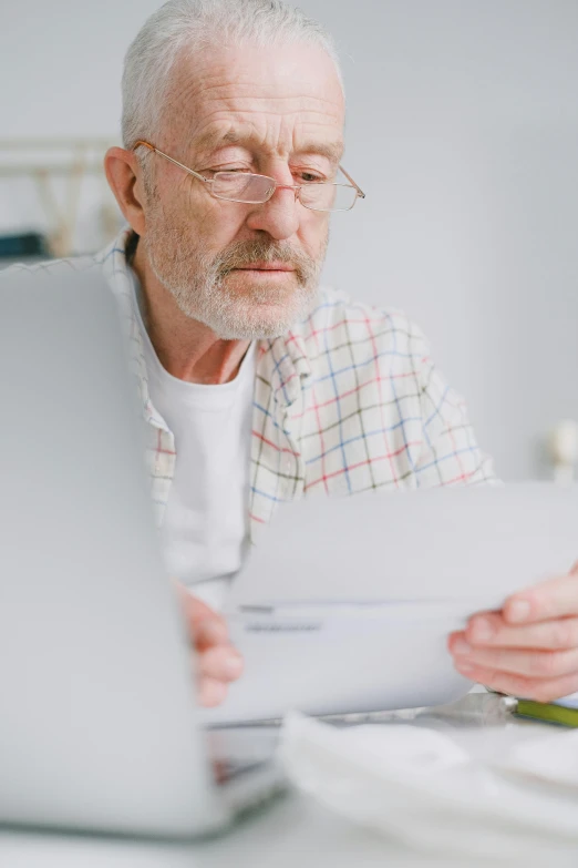 a man sitting at a table with a laptop and papers, gray beard, thumbnail, single subject, lgbtq