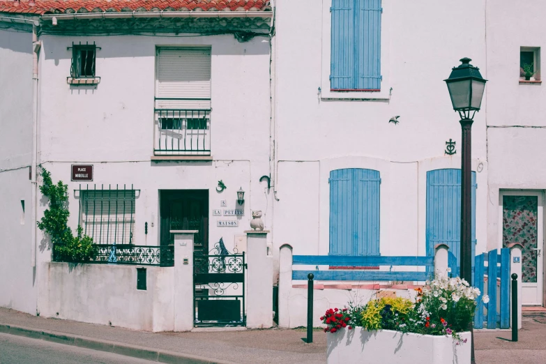 a white building with blue shutters and a blue bench, by Andrée Ruellan, pexels contest winner, art nouveau, small port village, animation, 1990's photo, french village exterior