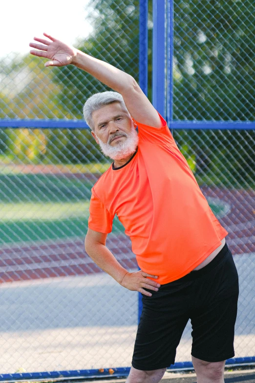 a man standing on top of a tennis court holding a racquet, pixeled stretching, white hair and white beard, wearing an orange t-shirt, soccer