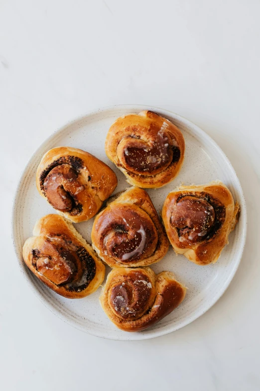 a plate of cinnamon buns on a white table, by Nina Hamnett, baroque, 6 pack, chocolate, woodfired, various sizes