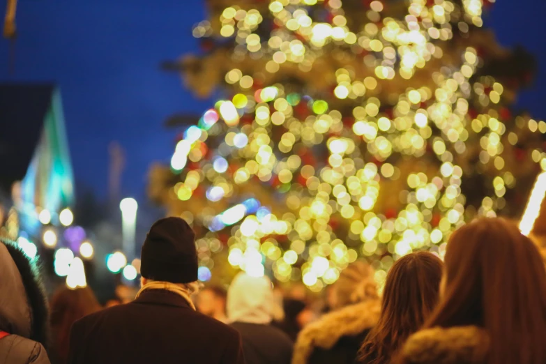 a group of people standing in front of a christmas tree, by Julia Pishtar, pexels, happening, crowded square, warm coloured, thumbnail