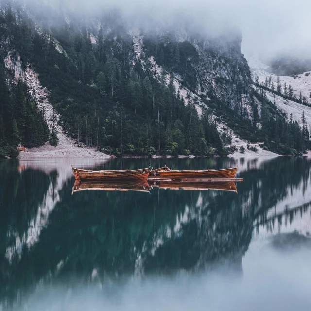 a couple of boats floating on top of a lake, by Sebastian Spreng, pexels contest winner, mountain water, wooden boat, alessio albi, cold but beautiful