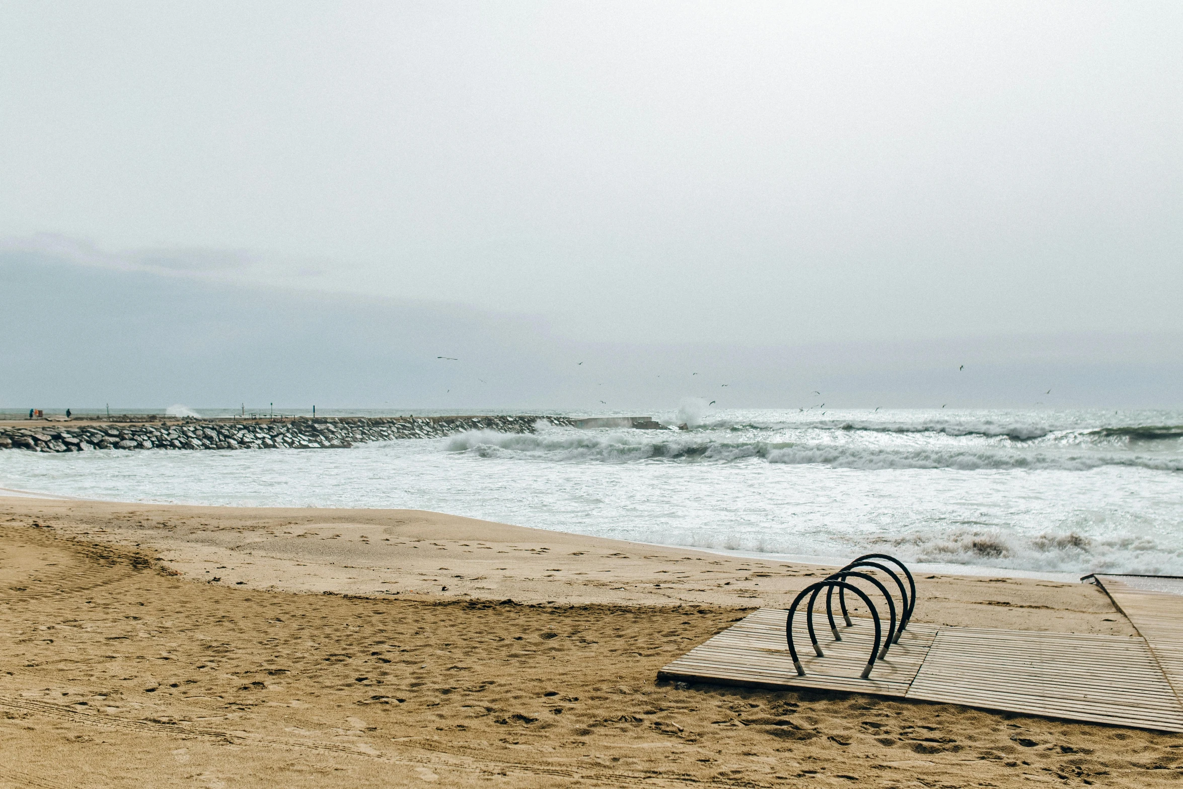 a bench sitting on top of a sandy beach next to the ocean, a picture, by Lucia Peka, unsplash, overcast day, boardwalk, tentacles rising from the sea, thumbnail