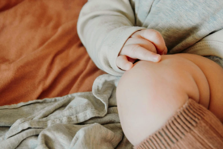 a baby laying on top of a bed covered in a blanket, trending on pexels, pregnant belly, earthy colours, holding hands, little boy wearing nun outfit