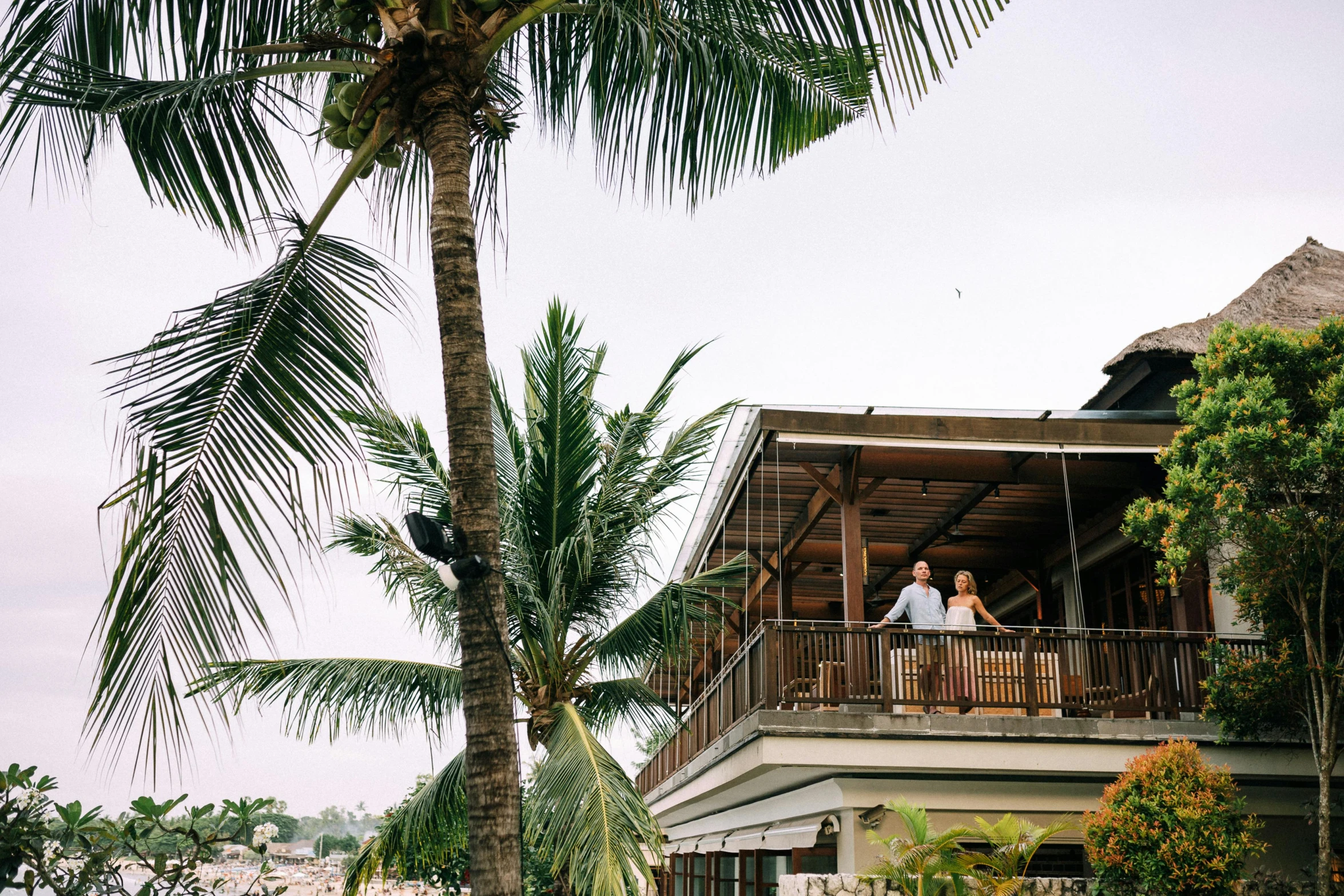 a couple of people standing on top of a balcony, coconut trees, lachlan bailey, al fresco, viewed from the ocean