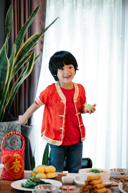 a little boy standing in front of a table full of food, inspired by Tang Di, shutterstock contest winner, red elegant shirt, bao pham, embroidered shirt, she is happy