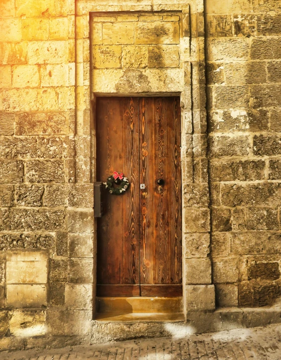 a wooden door sitting on the side of a stone building, an album cover, pexels contest winner, romanesque, religious, brown, cyprus, flowers around