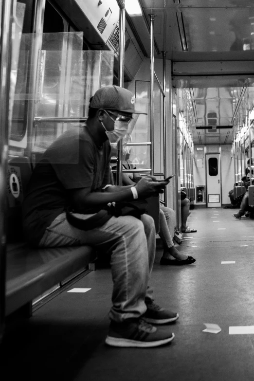 a black and white photo of a man sitting on a subway, wearing facemask, digital media, black man, cell phone photo