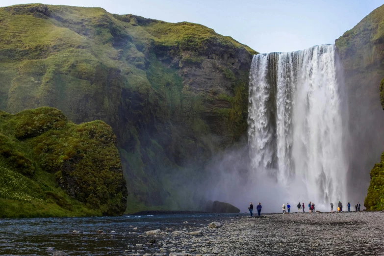 a group of people standing in front of a waterfall, by Jesper Knudsen, pexels contest winner, hurufiyya, panoramic shot, fan favorite, historical setting, viewed from a distance