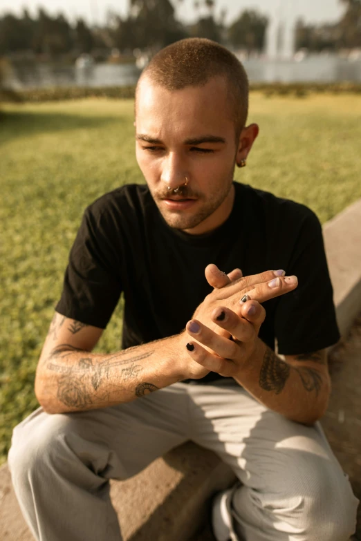 a man sitting on a ledge looking at his cell phone, a tattoo, inspired by Elsa Bleda, trending on pexels, hyperrealism, his palms are sweaty, brown buzzcut, sitting in a field of cannabis, photo of a hand jewellery model