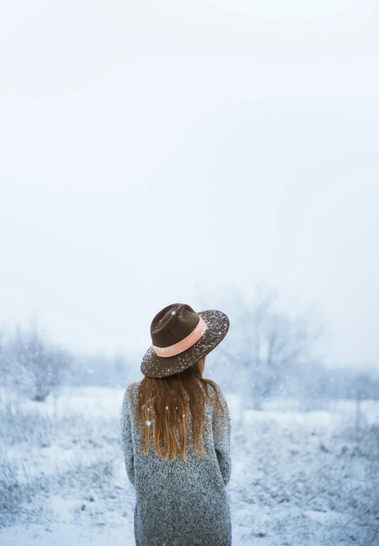 a woman standing in the snow wearing a hat, pexels contest winner, back, girl with brown hair, white sky, prints