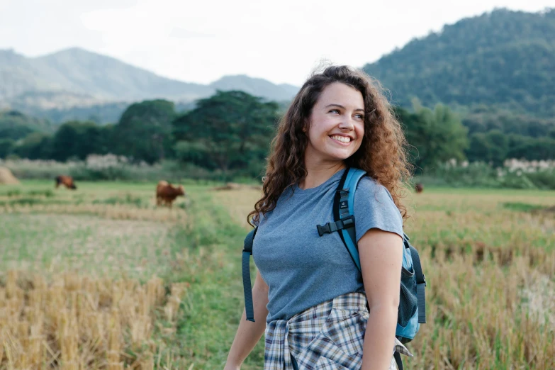 a woman with a backpack standing in a field, happening, profile image, smiling, avatar image, full shot photograph