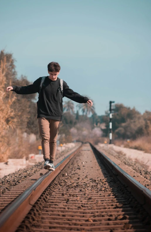 a man riding a skateboard down a train track, an album cover, unsplash, realism, posing for a picture, standing in road, low quality photo, male teenager
