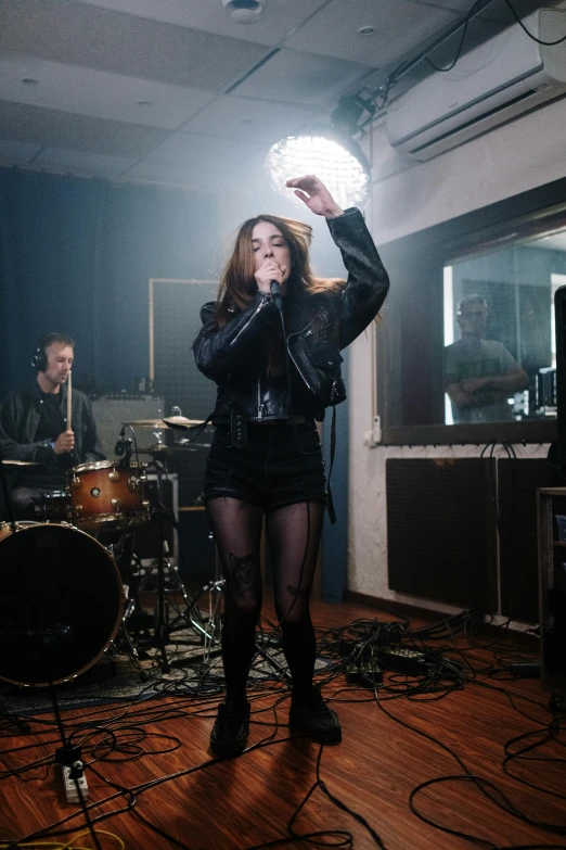 a woman in a black dress singing into a microphone, an album cover, inspired by Elsa Bleda, pexels contest winner, antipodeans, she wears leather jacket, warpaint aesthetic, performing a music video, indoor scene
