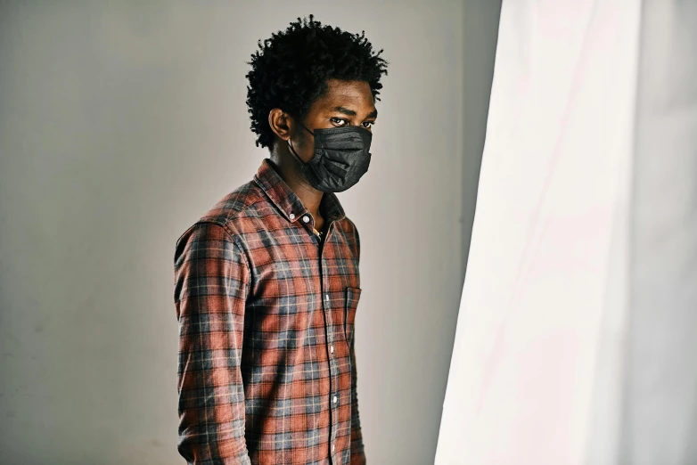 a man wearing a face mask standing in front of a curtain, inspired by Gordon Parks, visual art, in a photo studio, black main color, commercial, brown skinned