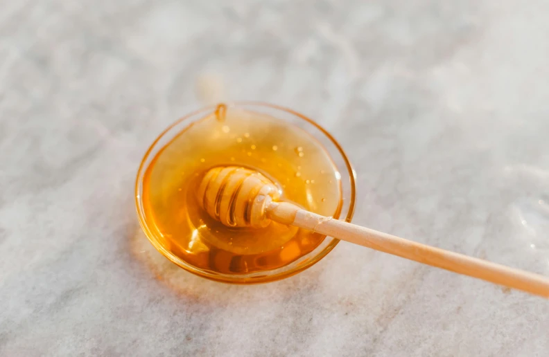 a glass of honey with a wooden stick sticking out of it, by Emma Andijewska, trending on pexels, on a marble pedestal, bowl, resin coated, hexagonal shaped