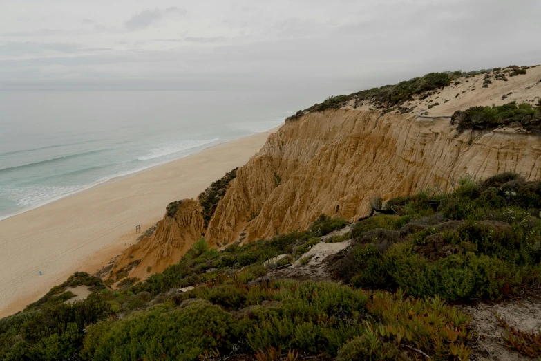 a man riding a surfboard on top of a sandy beach, an album cover, unsplash contest winner, australian tonalism, looking down a cliff, between sedimentary deposits, eucalyptus, road to the sea