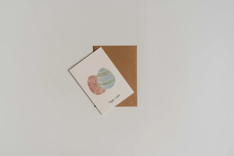 a card sitting on top of a brown envelope, by Jessie Algie, mingei, egg, high quality product photo, pebbles, multi - coloured