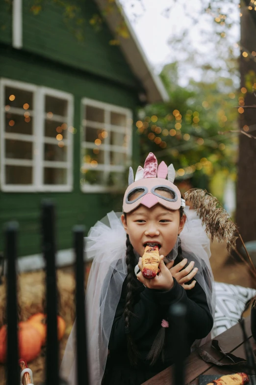 a little girl sitting at a table eating a donut, pexels contest winner, wearing a crown and cape, holding bat, taejune kim, eating outside