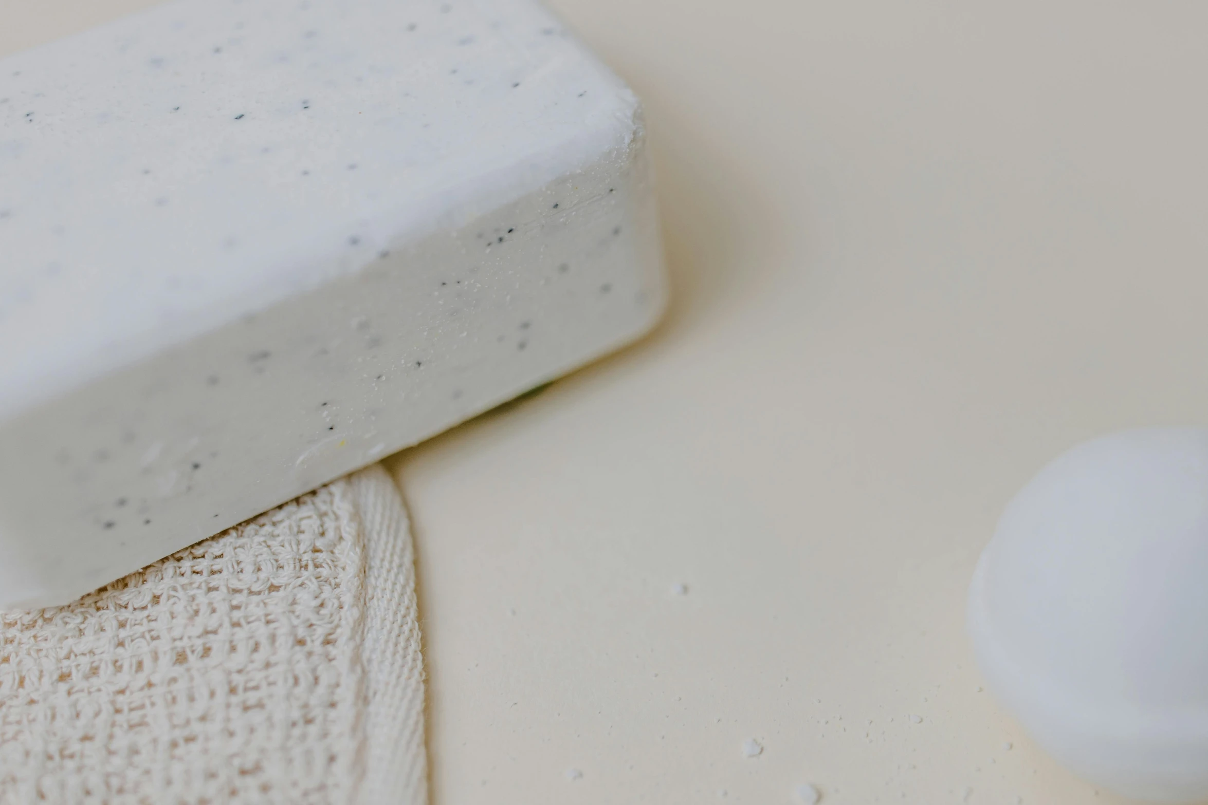 a soap bar sitting on top of a towel next to a ball of soap, by Emma Andijewska, trending on pexels, minimalism, white powder bricks, speckled, background image, sustainable materials