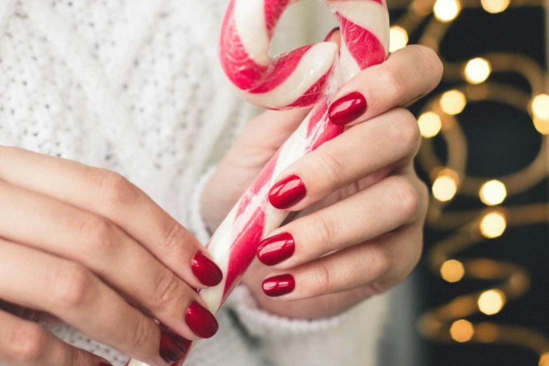 a close up of a person holding a candy cane, a photo, by Julia Pishtar, trending on pexels, nail polish, maroon red, getty images, made of candy