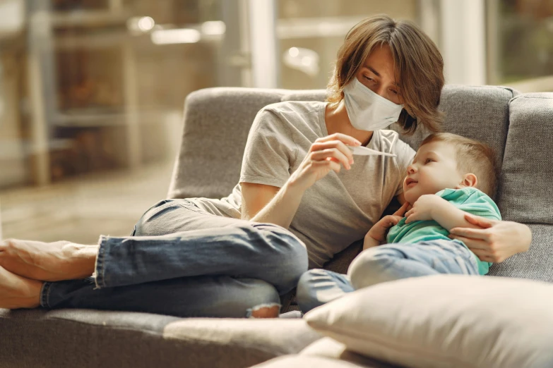 a woman sitting on a couch holding a baby, shutterstock, surgical mask covering mouth, instagram picture, australian, son