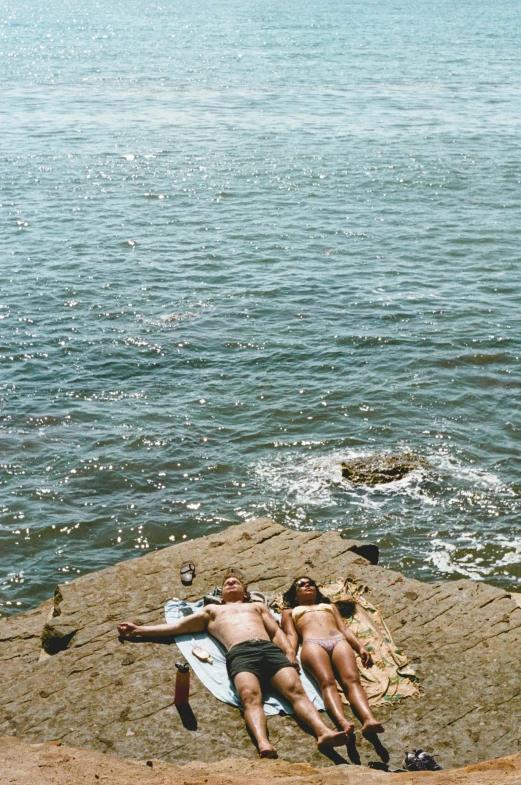 a group of people laying on top of a rock next to the ocean, by Ren Hang, renaissance, harbor, two men, sparkling in the sunlight, ( ( photograph ) )