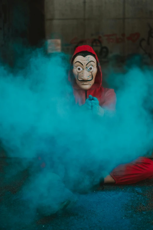 a man in a mask sitting on the ground, by Paul Bird, pexels contest winner, graffiti, red smoke, as a claymation character, red and cyan ink, man in a jester costume