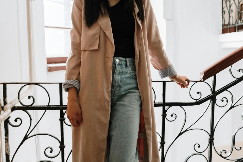 a woman standing on the stairs of a building, trending on pexels, light brown trenchcoat, jeans and t shirt, pink clothes, wearing a duster coat