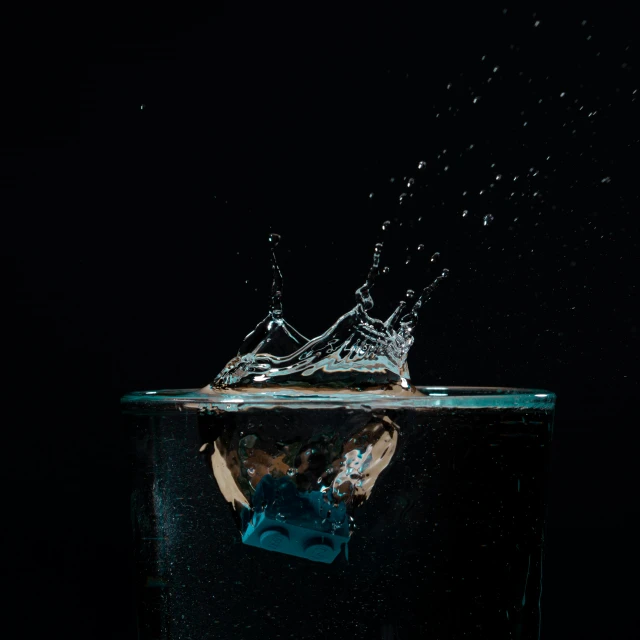 a glass filled with water sitting on top of a table, by Daniel Seghers, pexels, photorealism, black splashes, floating crown, water jets, taken with sony alpha 9