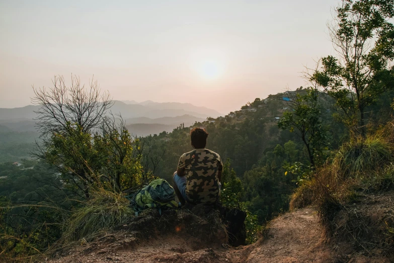 a man sitting on top of a hill next to a forest, pexels contest winner, uttarakhand, looking off into the sunset, secluded, view from back