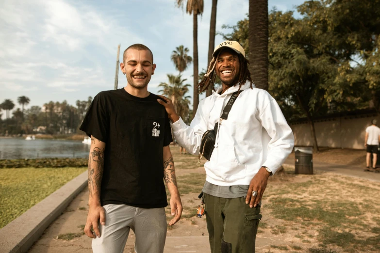 two men standing next to each other on a sidewalk, a photo, bladee from drain gang, smiling into the camera, los angeles, in a scenic background