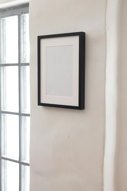 a picture frame hanging on a wall next to a window, inspired by Robert Mapplethorpe, black watercolour, with a white background, close up shot from the side, ( ( photograph ) )