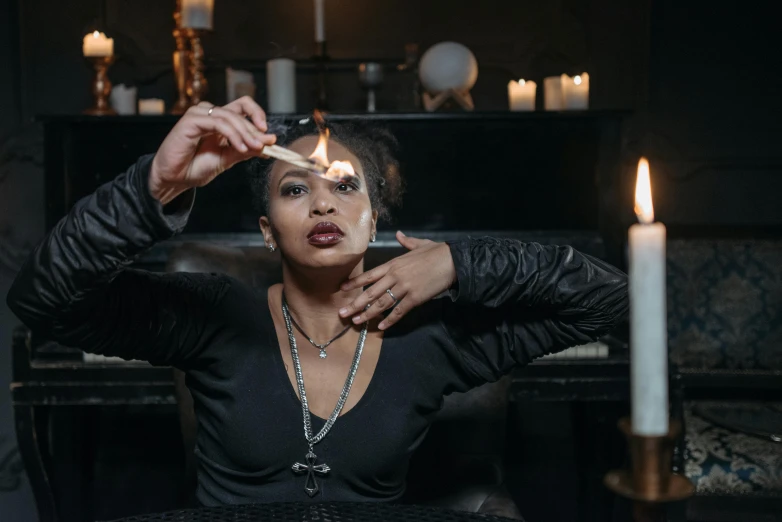 a woman sitting at a table with a lit candle, pexels contest winner, wearing gothic accessories, cardi b, casting a fire spell, ☁🌪🌙👩🏾