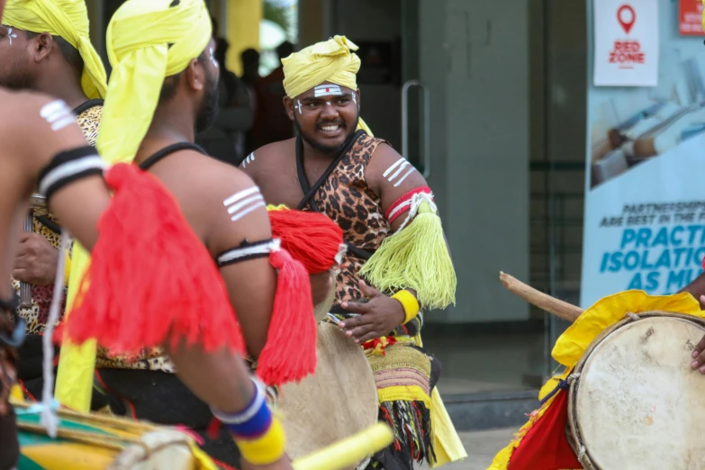 a group of men standing next to each other holding drums, pexels contest winner, hurufiyya, wearing a fancy dress, avatar image, sri lanka, people dancing in background