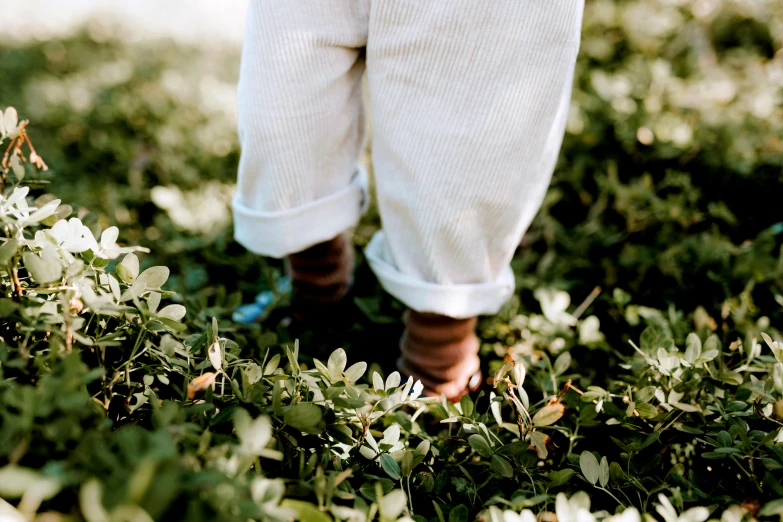 a person standing on top of a lush green field, an album cover, by Liza Donnelly, unsplash, green corduroy pants, toddler, wearing white pajamas, very close up foot shot