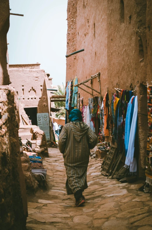 a person walking down a cobblestone street, les nabis, tattered cloth robes, desert robe, mud and brick houses, hanging