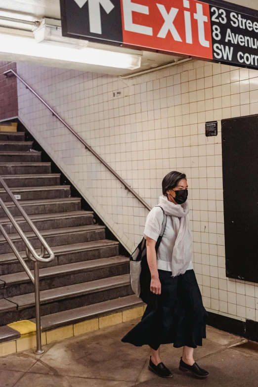 a woman wearing a face mask walks past a exit sign, an album cover, by Rafail Levitsky, mta subway entrance, asian male, 1 staircase, 🚿🗝📝