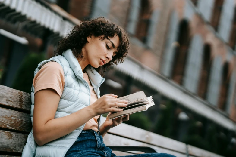 a woman sitting on a bench reading a book, a portrait, trending on pexels, happening, curly haired, college students, thumbnail, girl with brown hair