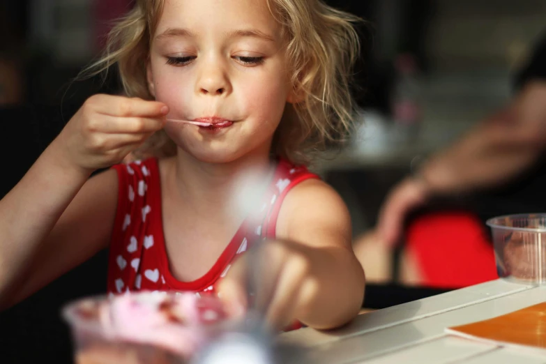 a little girl sitting at a table with a spoon in her mouth, pexels, made of candy, square, thumbnail, diner caffee