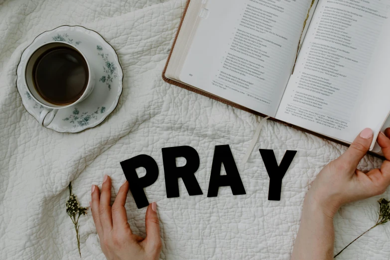 a person laying on a bed with a book and a cup of coffee, trending on pexels, hurufiyya, prayer hands, unreadable text, nun outfit, realistic »