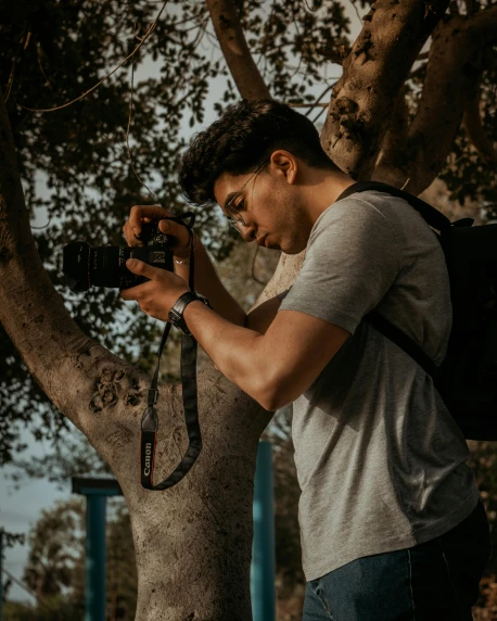 a man taking a picture of a tree with a camera, by Robbie Trevino, a man wearing a backpack, close up portrait photo, cinematic outfit photo