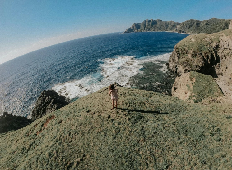 a person standing on top of a hill next to the ocean, islandpunk, pov photo