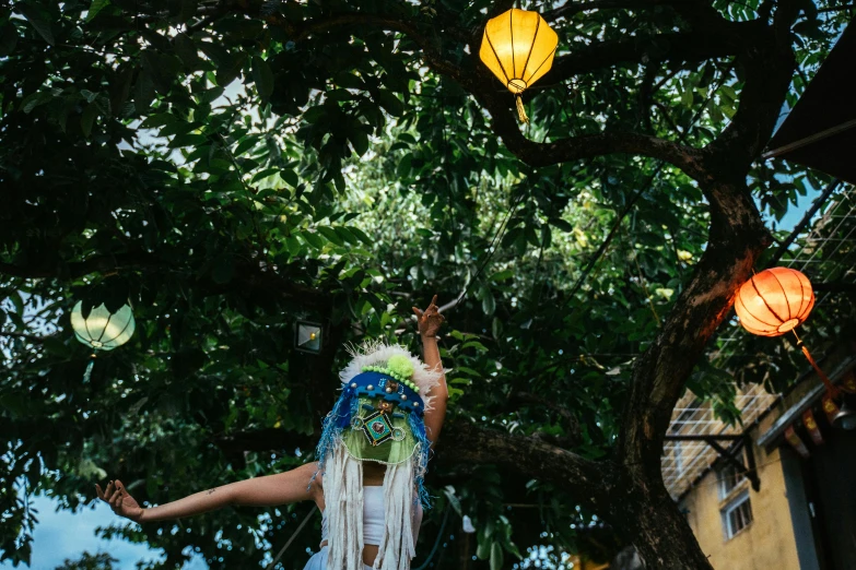 a woman that is standing in front of a tree, by Liza Donnelly, unsplash, process art, hanging lanterns, feathered headdress, puppet on a string, taiwan