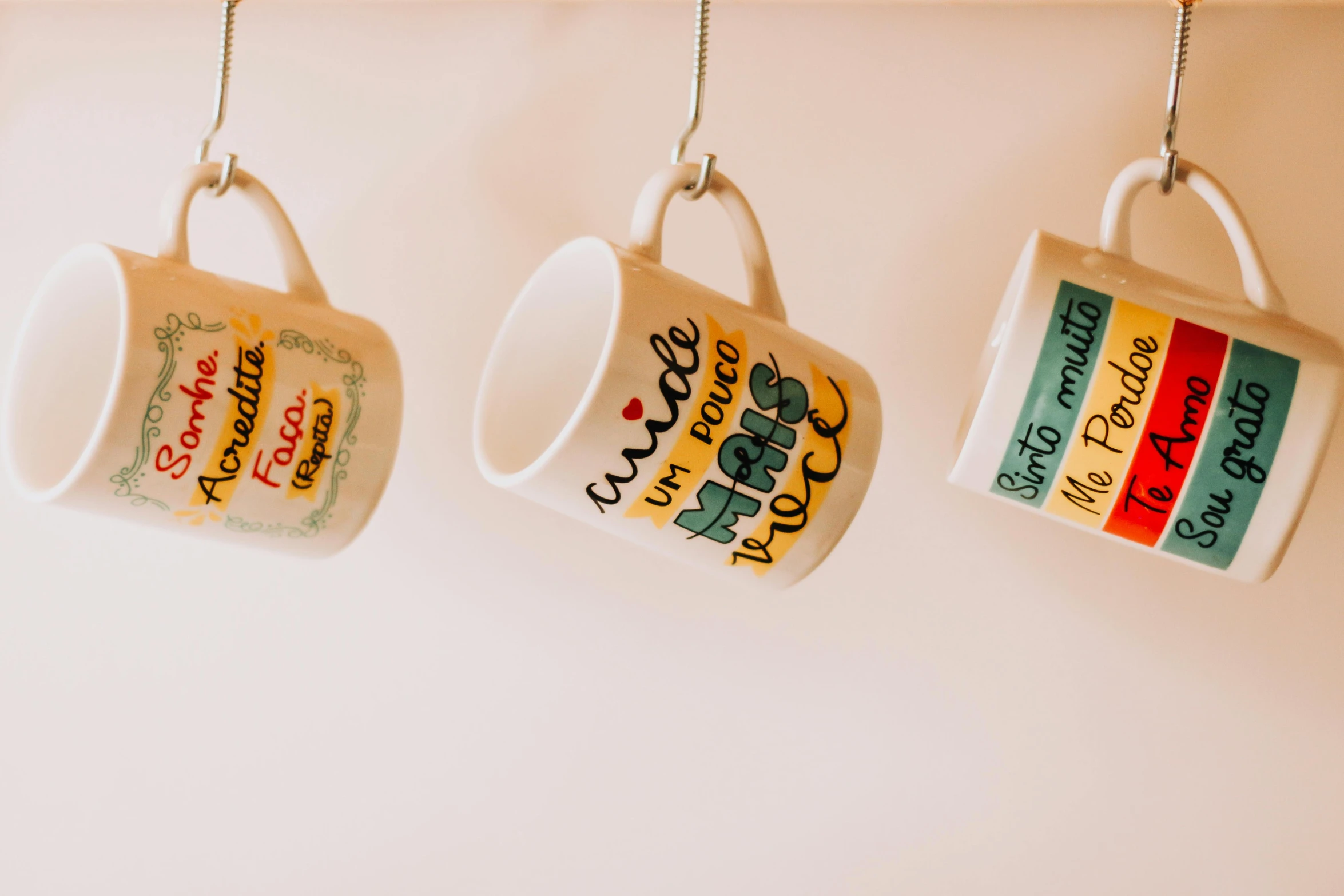 three coffee mugs hanging on a wall, a cartoon, trending on pexels, emma bridgewater and paperchase, eye level view, with names, closeup - view