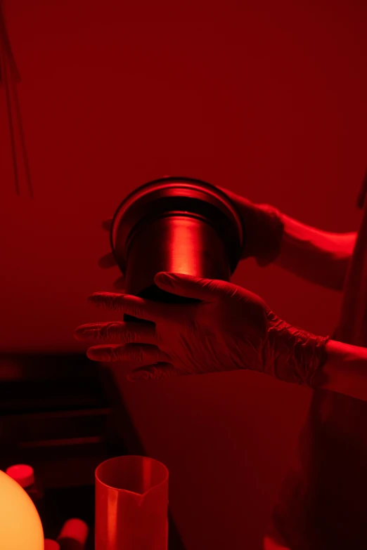 a person in a room with a red light, coating a stubborn core.', holding a tin can, darkroom, promo image