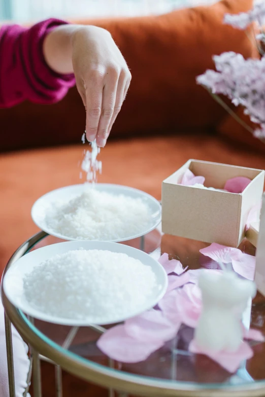 a woman sitting on a couch next to a coffee table, a still life, inspired by Cui Bai, trending on unsplash, close up of single sugar crystal, falling petals, ingredients on the table, spa