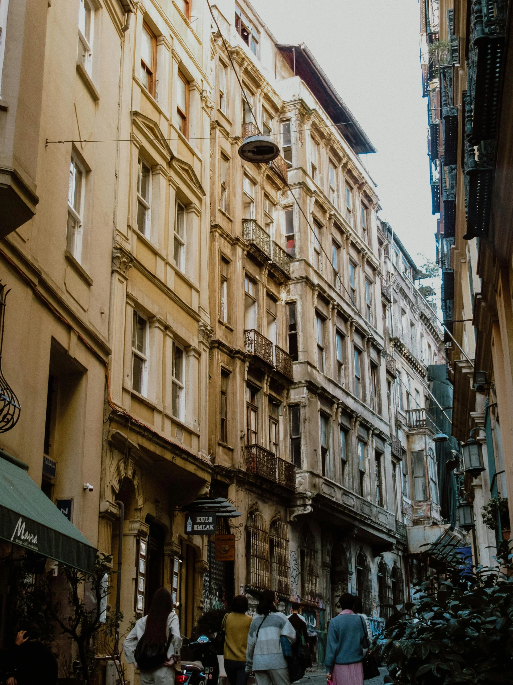 a group of people walking down a street next to tall buildings, a photo, inspired by Niyazi Selimoglu, pexels contest winner, renaissance, old apartment, brown, mediterranean architecture, profile image