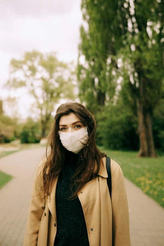 a woman wearing a face mask in a park, a picture, by Adam Marczyński, trending on pexels, renaissance, wearing jacket, lorde, standing in road, 256435456k film