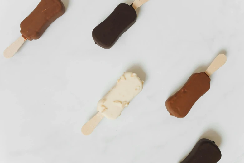 a group of pops sitting on top of a counter, cream white background, fully chocolate, dark sienna and white, giant wooden club